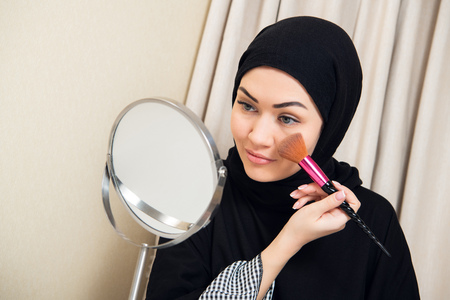 Arab woman applying makeup on her face, wearing traditional Arabian dressの写真素材