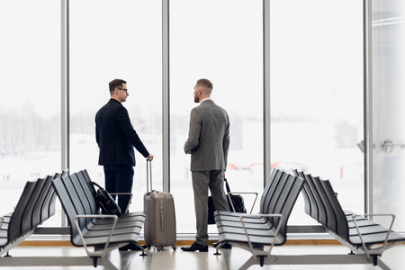 Silhouette of two businessman standing in front of a big window at airport at wating area near departure gateの写真素材