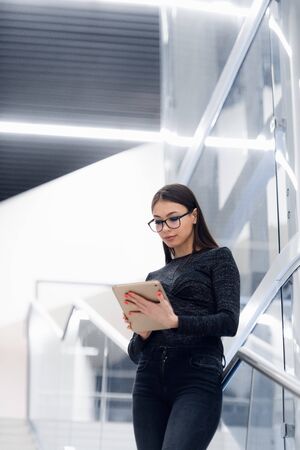 Technology, business and corporate concept - happy woman or student with tablet pc computer standing on stairs at modern building.の写真素材