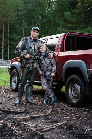 Father and son came to the forest for hunting together. Standing with a shotgun rifle in front of...