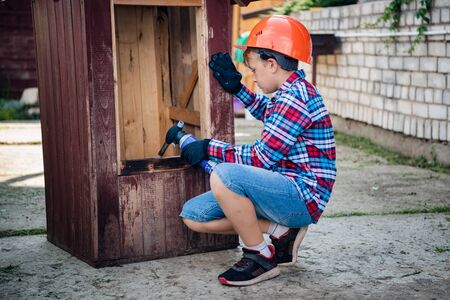 Boy burns the wall of a wooden house. son helps parents with painting the garden houseの写真素材