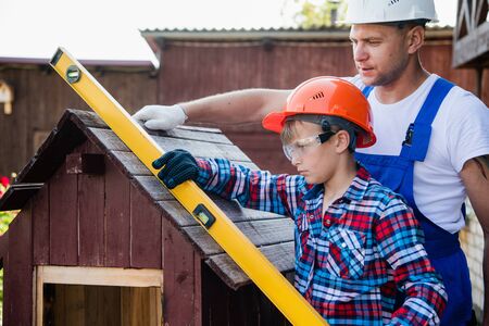 The boy holds the building level, checking the accuracy of the dog house roof.