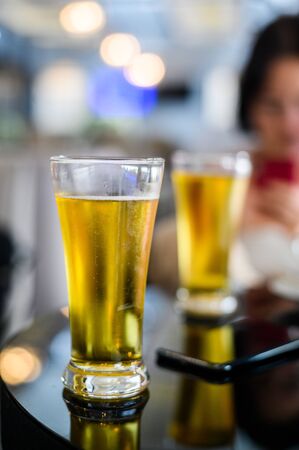 Glass of beer in bar and mobile phone on a tableの写真素材