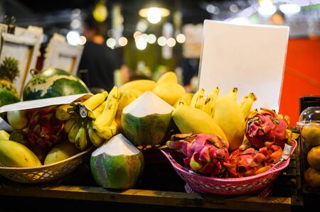 Tropical thai fruits stall at local food market in Thailand. Coconut, dragonfruit, banana and mango at night fair.の写真素材