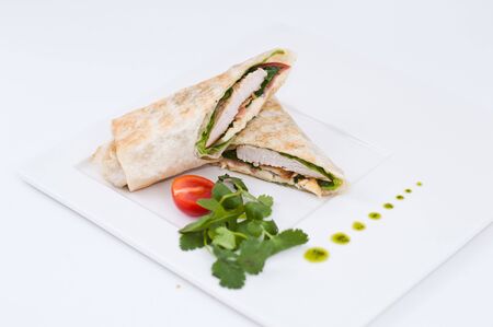 Shawarma chicken roll in a pita with fresh vegetables and cream sauce on white background. Selective focusの写真素材