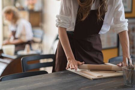 Female hands flatting piece of clay lying on fabric using wooden rolling pin in ceramic studio.の写真素材