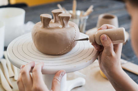 Closeup of bottom of mug, which is being decorated in ceramic studio. Female professional hands making clay dots or drops on the surface of vase by special squeezing tool.の写真素材