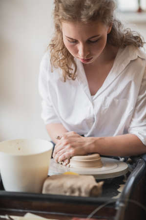 Female potter working with clay on wheel in studio. Clay with water splattered around the potter wheel.の写真素材