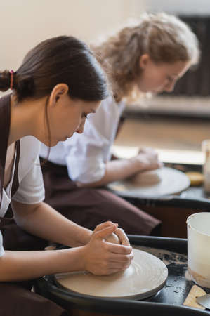 Two female ceramic artists in apron using clay material working in potter studio. Evening freelance distance learning. Adult hobby adventure. Winter educating leisure. Training in modern workshop.の写真素材