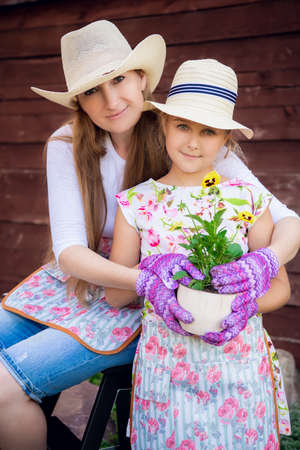 Woman and girl, mother and daughter, gardening together planting flowers in the garden. Looking at cameraの写真素材