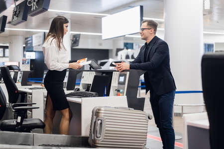 Business trip. Handsome young businessman in suit holding his passport and talking to woman at airline check in counter in the airportの写真素材