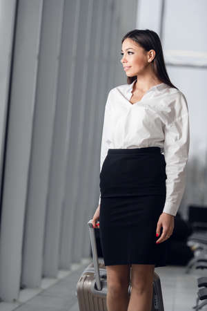 Portrait of a young business woman in smart clothes walking along hotel lobby with her suitcaseの写真素材