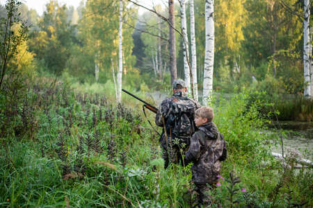 Fathers day. Father with gun showing something to son while hunting on a nature. Happy family, Fathers Day and local summer vacationの写真素材
