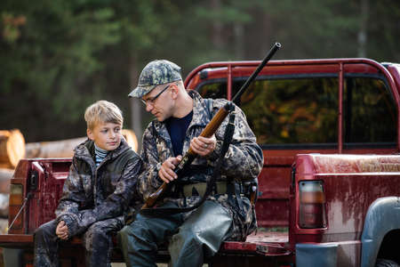 Father in a cap and his son sitting in a car after the hunt.の写真素材