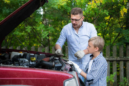 Dad and his son repairing car with open hood outdoors, fixing engineの写真素材