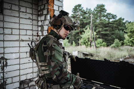 Military man with gun case takes out an assault rifle in destroyed city. Military and rescue...