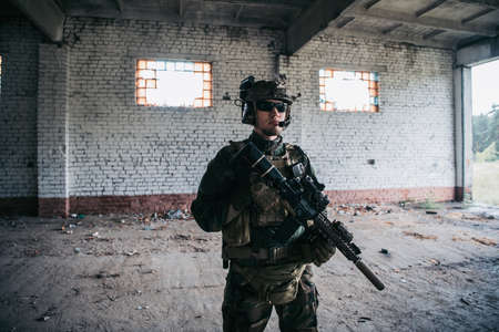 Military man with assault rifle standing inside building, he is ready for combatの写真素材