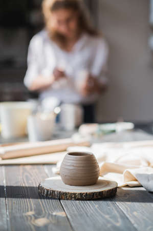 Newly made on a pottery wheel clay pot on a wooden table. Woman paint the ceramic on a background in a pottery studio.の写真素材