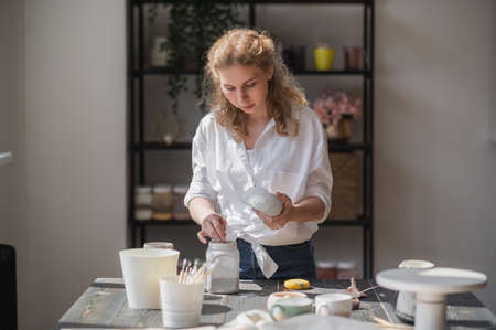 Female potter glazing raw unburned ceramic cup using brush. Earthenware mug putting colorant on pottery workshop.の写真素材