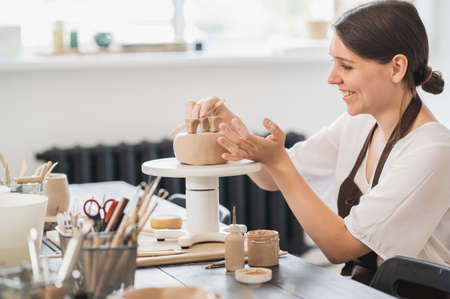 Close up of female potter holding stick and making ornament on earthenware. Clay master moulding clay product. Concept of ceramic art and hobby.の写真素材