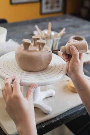 Close up of female potter holding stick and making ornament on earthenware. Clay master moulding clay product. Concept of ceramic art and hobby.の写真素材