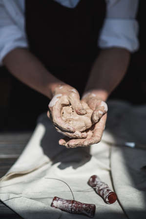 Close up of woman hands works with clay. Female potter kneads and moistens the clay before work.の写真素材