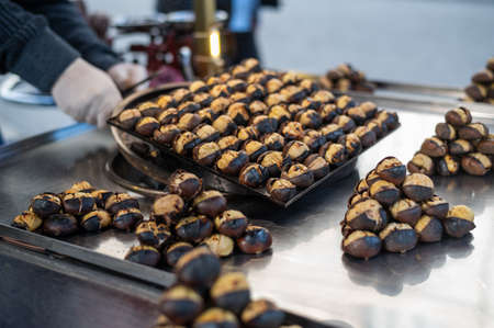 Male salesman is cooking Roasted chestnuts on a city street. Street food, hot cooked chestnutsの写真素材