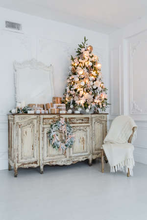 Christmas tree on wooden chest of drawers commode bureau in white interior, decorated with artificial flowers, garlands and toysの写真素材