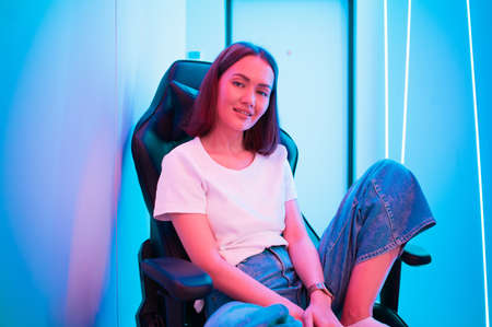 Streamer girl relaxing sitting on a gaming chair after live stream. Room with colorful neon light.の写真素材