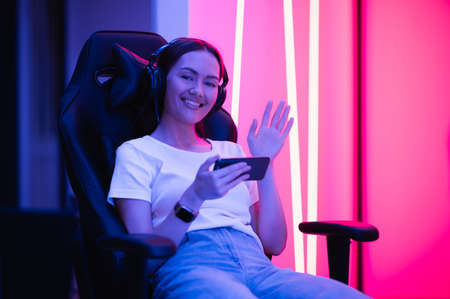 Girl relaxing playing games on mobile phone and sitting on a gaming chair. Room with colorful neon light.の写真素材