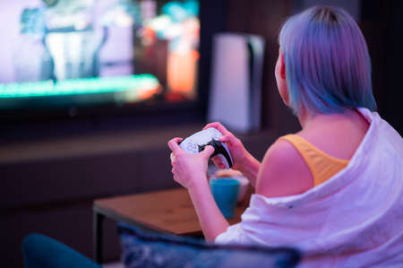 Moscow - November 28 2020: Woman holding new Dualsense controller joystick of Sony PlayStation 5 gaming console at home. Playing games with her boyfriend.のeditorial素材