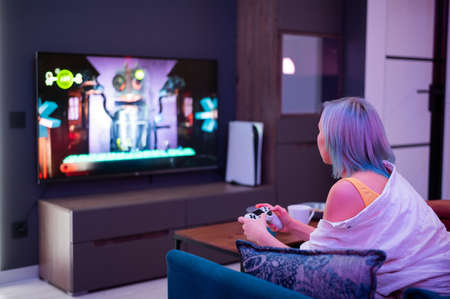Teenager girl with colorful blue and pink hair hold joystick and play video games at home at night.の写真素材