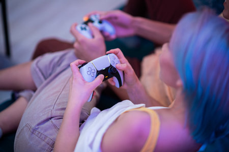 Young couple playing video games while sitting on the living room floor lit with neon color.