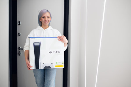 Happy excited woman comes home to make a surprise for her boyfriend with a brand new Sony PlayStation 5 gaming console she bought for christmas. Moscow - November 28 2020のeditorial素材