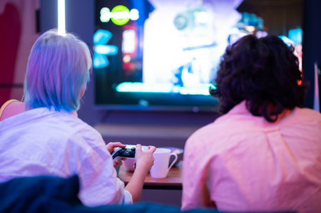 Happy couple playing video games at home during self isolation on a pandemic quarantine. Young man and woman love to spend time together. Back view.の写真素材