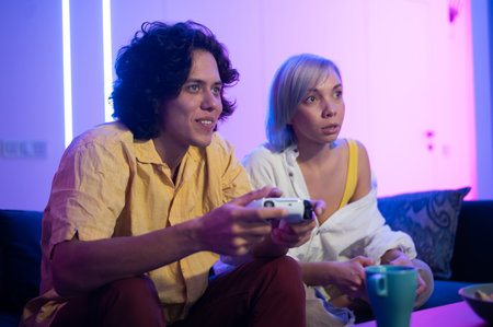 Young cheerful Caucasian husband and wife play videogames against each other at home enjoying leisure timeの写真素材