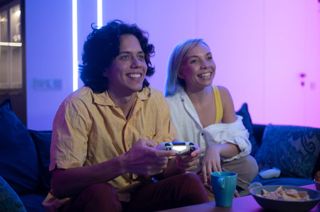 Happy young people playing video games on console while sitting on couch in front of tv. Millennial...