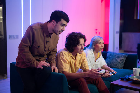 Young friends play video games while sitting on a couch in a living room.の写真素材