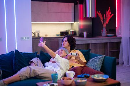 Girl streaming live on internet with mobile phone how she spending her time with boyfriend during self isoltaion at home. Man playing video games on gaming console.の写真素材