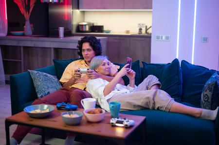 Happy young couple playing a video game sitting at home on a sofa during self isolation on quarantine.の写真素材