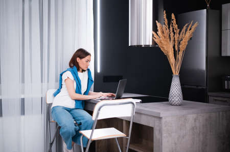 Happy young beautiful woman using laptop working remotely while sitting at home kitchen.の写真素材