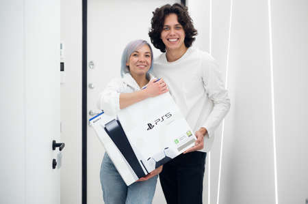 Woman surprises her brother with a next gen Sony playstation 5 console, online shopping present, modern video game device for cyber sport. Moscow - November 28 2020.のeditorial素材