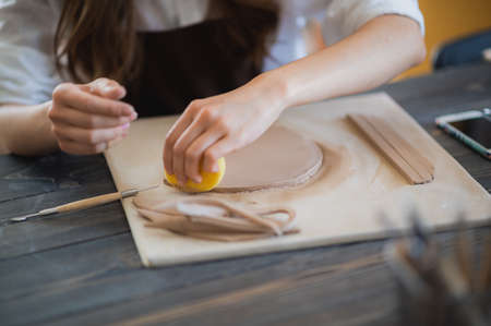 Artisan female potter prepares material for her pottery. Woman hands attach clay part to future ceramic product. Work close-up.の写真素材