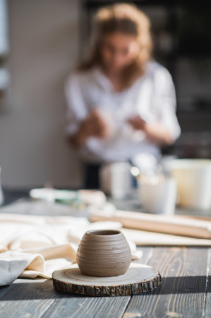 Close-up of a woman potter sculpts a brown clay pot on the background of a wooden table in the workshopの写真素材