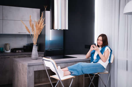 Shopping or ordering delivery online with mobile smart phone. Happy young woman using cellphone at home while sitting on a kitchen.の写真素材