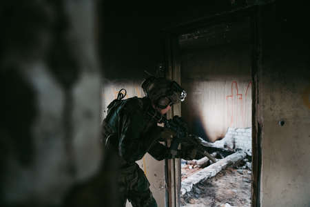 Military man with assault rifle standing inside building, he is ready for combat