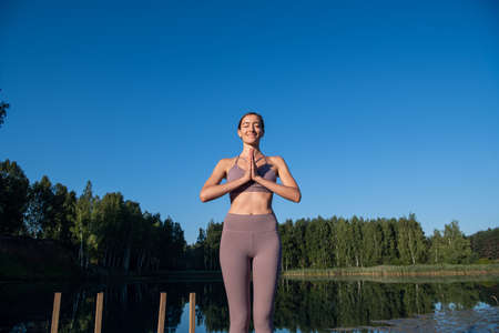 Yoga outdoor asana practice at sundown on a pier at a lake by sport calm girl.の写真素材