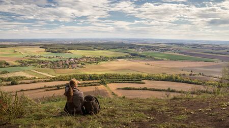 woman - hiker looks into valley on rural landscape with village, blue sky with white clouds, view from Rip mountain, Czech republicの写真素材