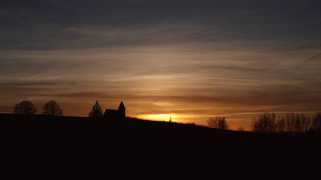 Panorama with silhouette of church and sun setting and golden-colored skyの写真素材