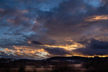 Beautiful sunset - red sky over hilly landscape, blue sky with orange-colored cloudsの写真素材